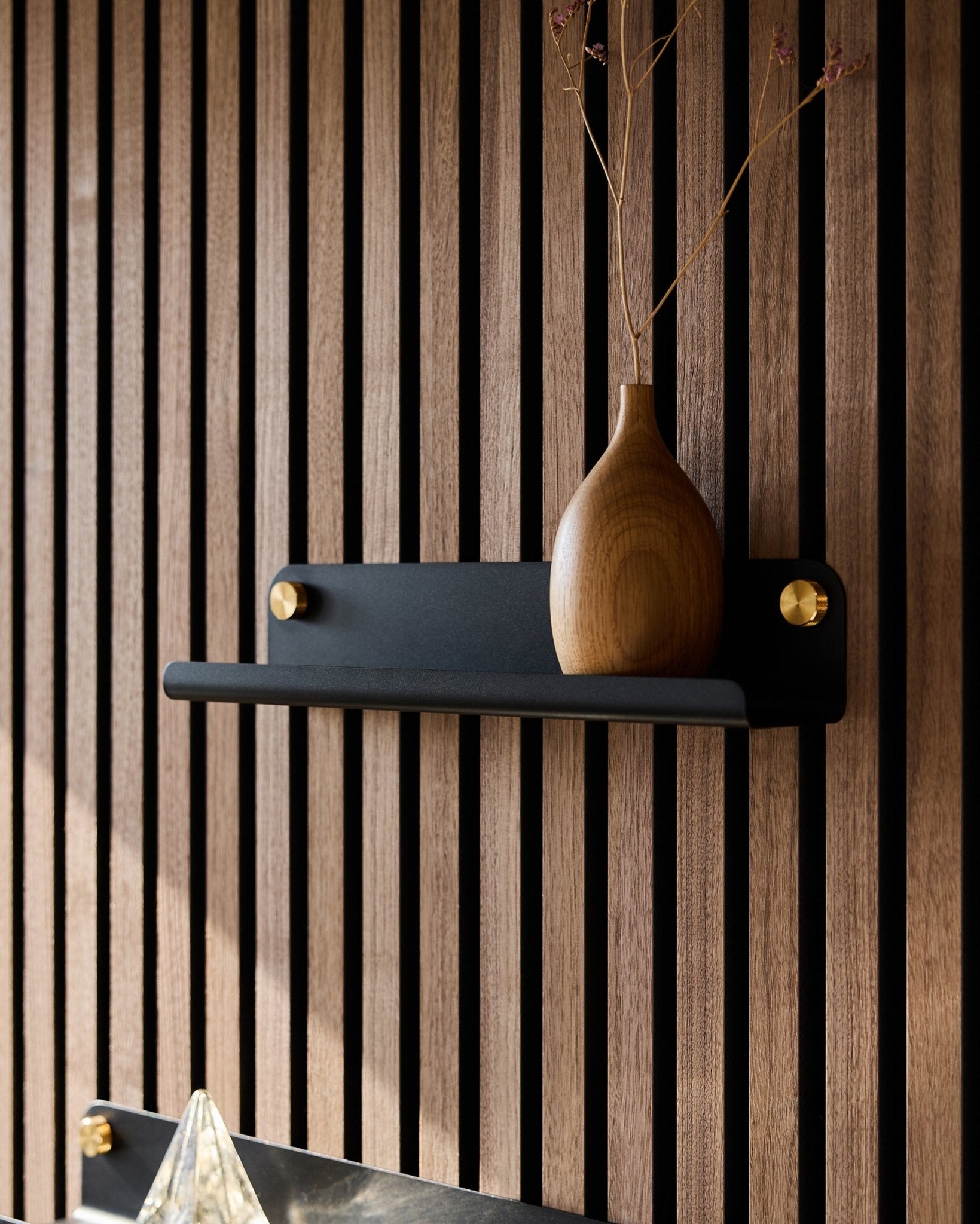 Eine Holzvase mit getrockneten Zweigen auf einem black WoodUpp Norr Narrow Shelf (35,9 cm), vor einer akustischen Slatwall-Paneele im vertical nordischen Stil.